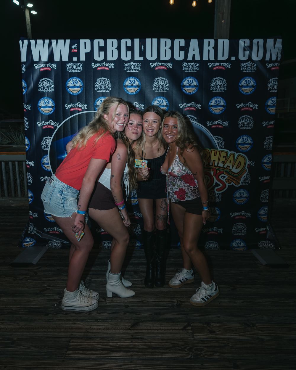 Four friends leaning in together in front of the PCB Club Card backdrop at Hammerhead Fred's
