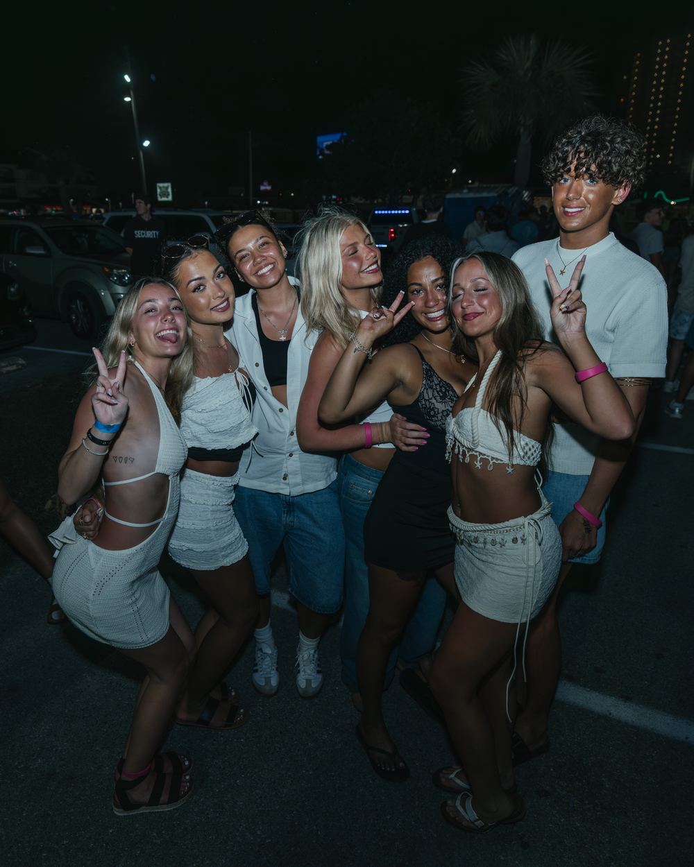 A crew of friends throwing peace signs in a parking lot on a spring break night in Panama City Beach