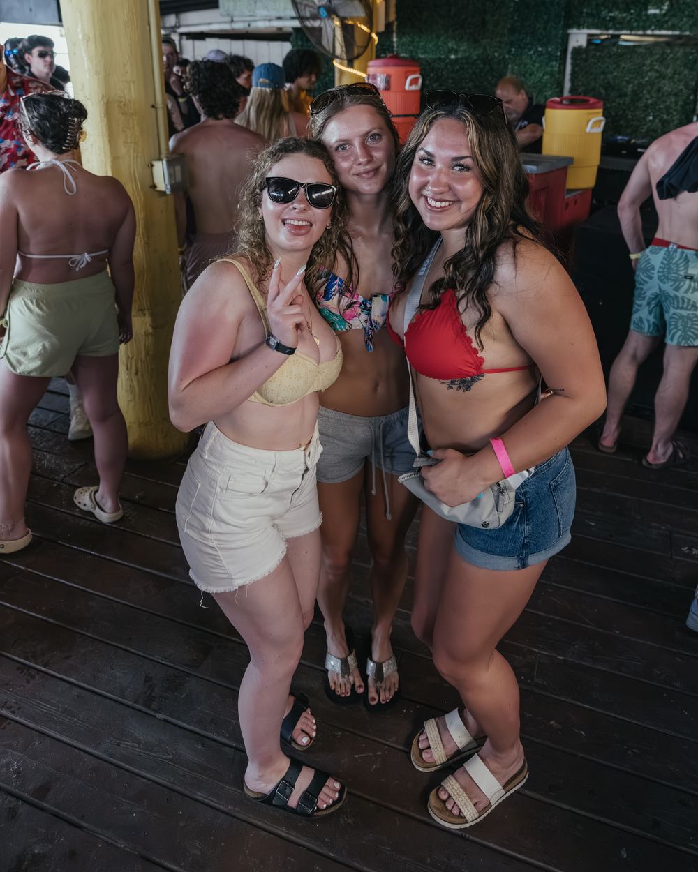 Three friends in swimsuits smiling together at a spring break day party in Panama City Beach